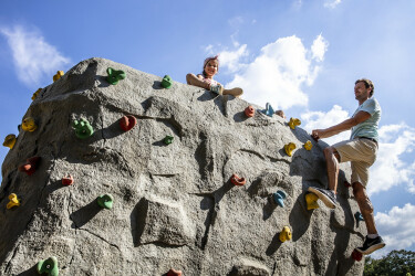 Vater und Tochter klettern bei Sonnenschein auf dem Boulderfelsen.