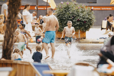 Kinder und Erwachsene in Badehosen spielen und rennen in der Wasserfläche des Himmelsspiegels.