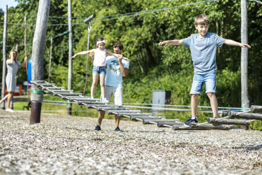 Eine junge Familie klettert über eine niedrige Hängebrücke im Seilgarten.