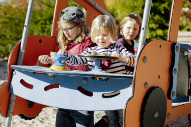 Drei Kinder spielen in einem Spielgerät, das aussieht wie ein Auto.