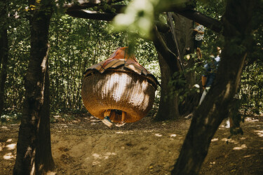 Kinder schaukeln in der geschlossenen Nestschaukel auf dem Waldspielplatz. Aus der Schaukel schauen nur die Füße heraus.