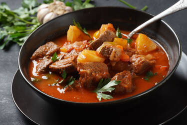 Dunkle Schale mit pikanter Gulaschsuppe mit Rindfleisch, Kartoffeln und Paprika.
